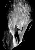 Black and white image of silhouetted caver with flowing water cascading from roof in front of them