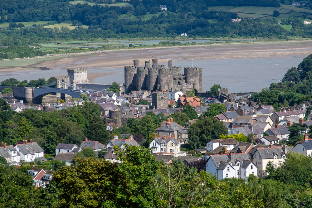 Image of a large medieval stone castle with rounded turrets (Conwy Castle) and town, with river behind.