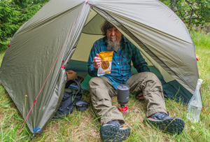 Image of man sat in tent holding up packet of 5 minutes to Delhi freeze-dried food